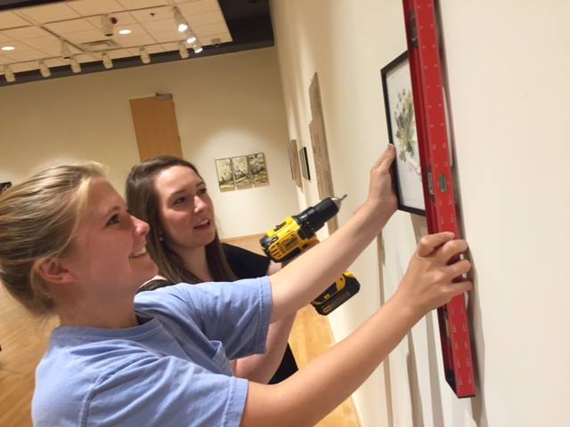 Student interns install art in the Staniar Gallery.